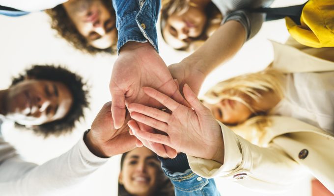 Hands of a multi-ethnic group of friends joined together as a sign of support and teamwork. Young people having fun together.