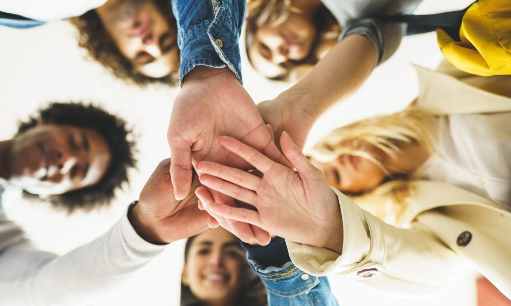 Hands of a multi-ethnic group of friends joined together as a sign of support and teamwork. Young people having fun together.