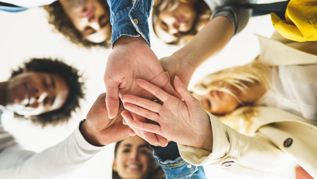 Hands of a multi-ethnic group of friends joined together as a sign of support and teamwork. Young people having fun together.